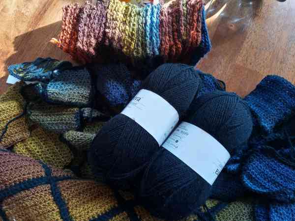 Many crocheted squares, some loose, some stitched together with a black border, and two balls of black yarn needed to complete the project