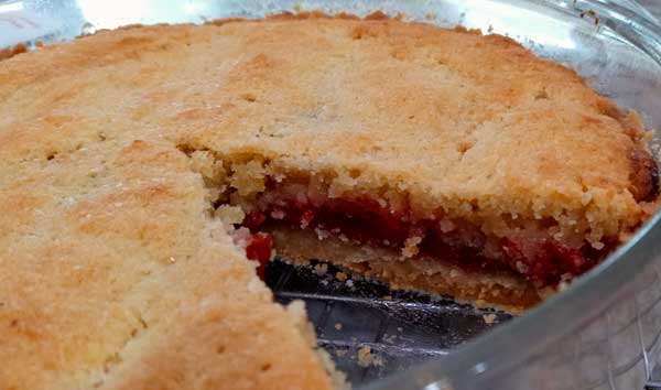 Cross section of a tart with a shortbread crust, a thin layer of red cherry filling, and and a cakey topping made with almond flour.