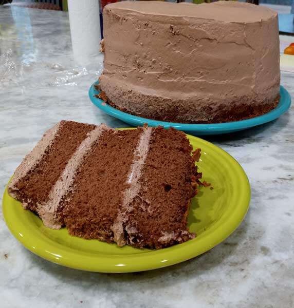A 3-tiered slice of chocolate cake with fluffy whipped frosting lying on its side, completely covering a dessert plate.