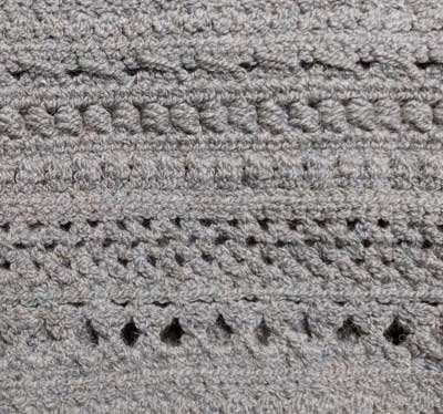 Closeup of stitches, including diagonal slashes, a row of beads like an abacus, slightly puffed clusters, a few rows of lattice, and large teardrop-shaped holes.