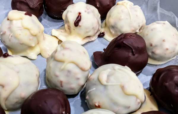 A collection of blob-shaped candies, some coated in dark chocolate, some coated in a pale substance lumpy with toasted coconut.