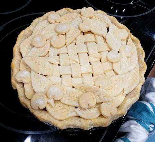 Unbaked pie decorated with lattice, leaves, and cherries made of dough.